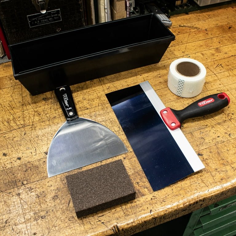 Essential drywall repair tools laid out on a work surface